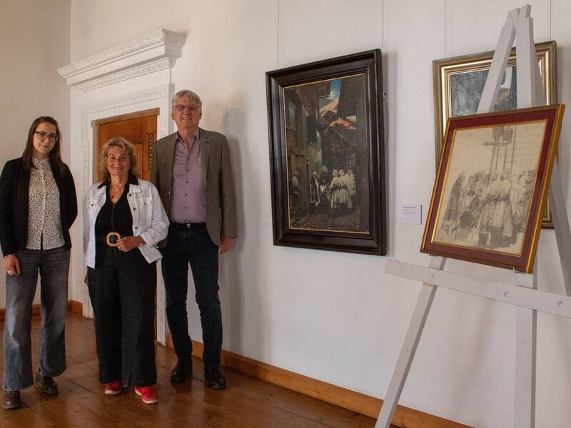 Das Foto zeigt (von links) Dr. Isabelle Schwarz (Leiterin Städtische Museen), Eva Kappelmeier-Gentile, die dem Museum die Skizze geschenkt hat, und Dritten Bürgermeister Wolfgang Bader. Sie befinden sich in einem prunkvollem Raum im Hohen Schloss zu Füssen; im Vordergrund ist die Skizze zu sehen, an der Wand hängt das finale Bild.